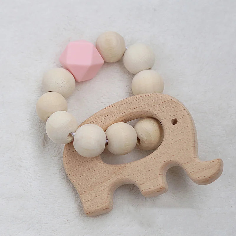 Wooden elephant-shaped baby teether with beaded ring, featuring natural wood and one pink polygon bead. Set on a soft white background.