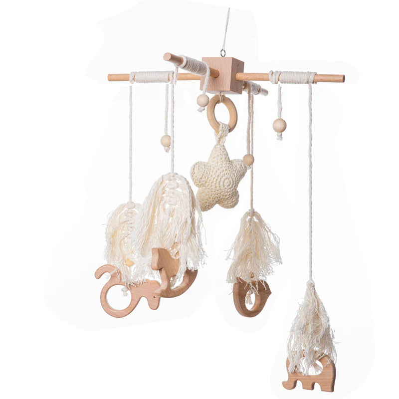 Wooden baby mobile with a minimalist design. Features hanging stars and animal shapes with cream tassels on strings, suspended from a wooden frame.