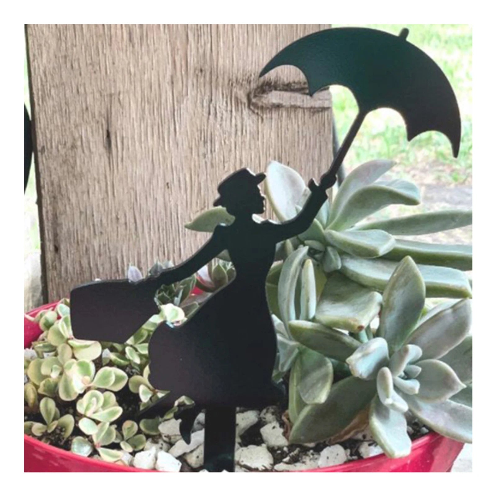 Silhouette of a woman holding an umbrella and bag in a red planter with succulents, set against a wooden background.