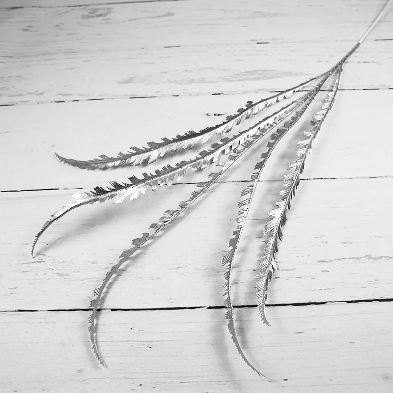 Silver metallic leaves with jagged edges laid on a rustic white wooden surface, creating a textured contrast between the shiny leaves and the matte background.