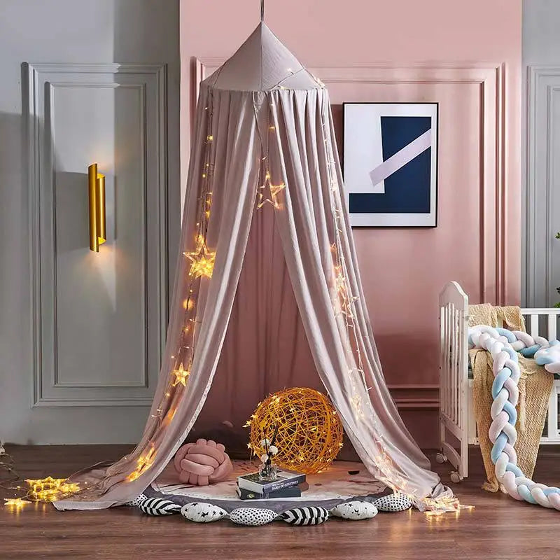 A cozy nursery corner features a canopy draped with starry string lights, a round yellow lattice lamp, cushions, books, and a braided crib bumper, set against pastel walls.