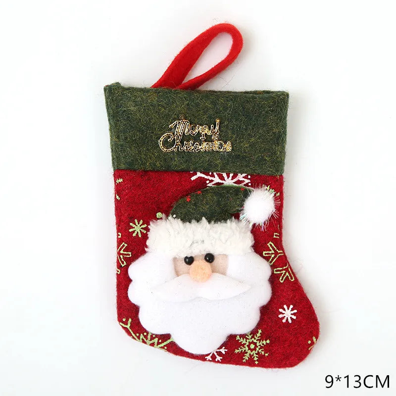 Small decorative Christmas stocking, red with gold "Merry Christmas" text and Santa design. White snowflake patterns. Green top and red hanging loop. Dimensions: 9x13 cm.