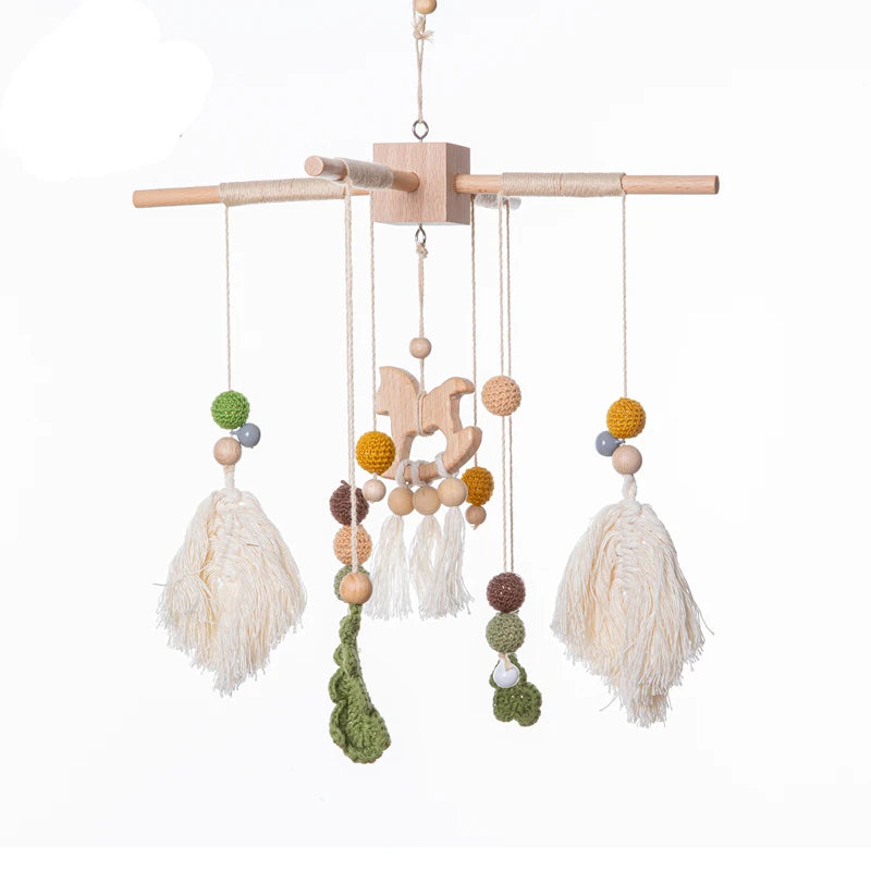 Wooden baby mobile with hanging elements including a rocking horse, tassels, crochet beads, and wooden balls in earthy tones, suspended from a cross frame.