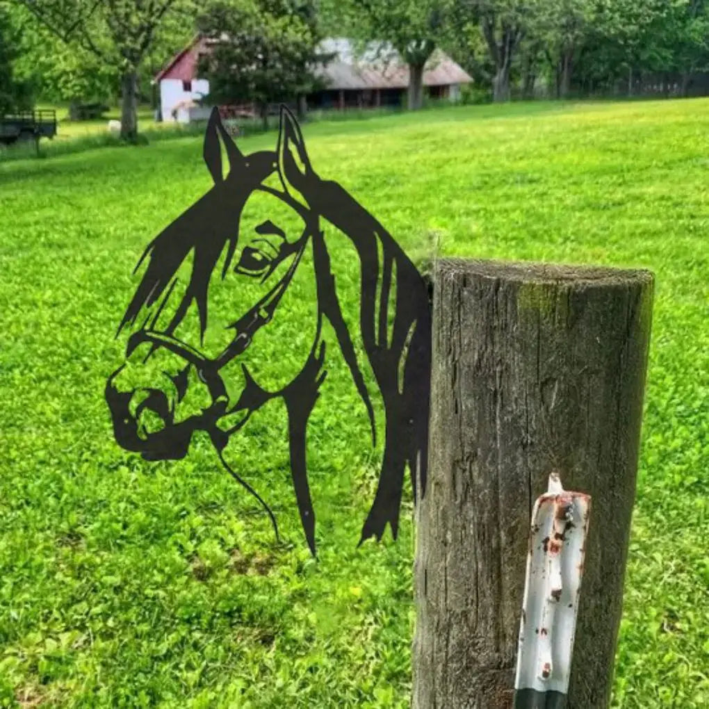 Silhouette of a horse's head on a wooden post in a lush green pasture, with trees and a barn in the background.