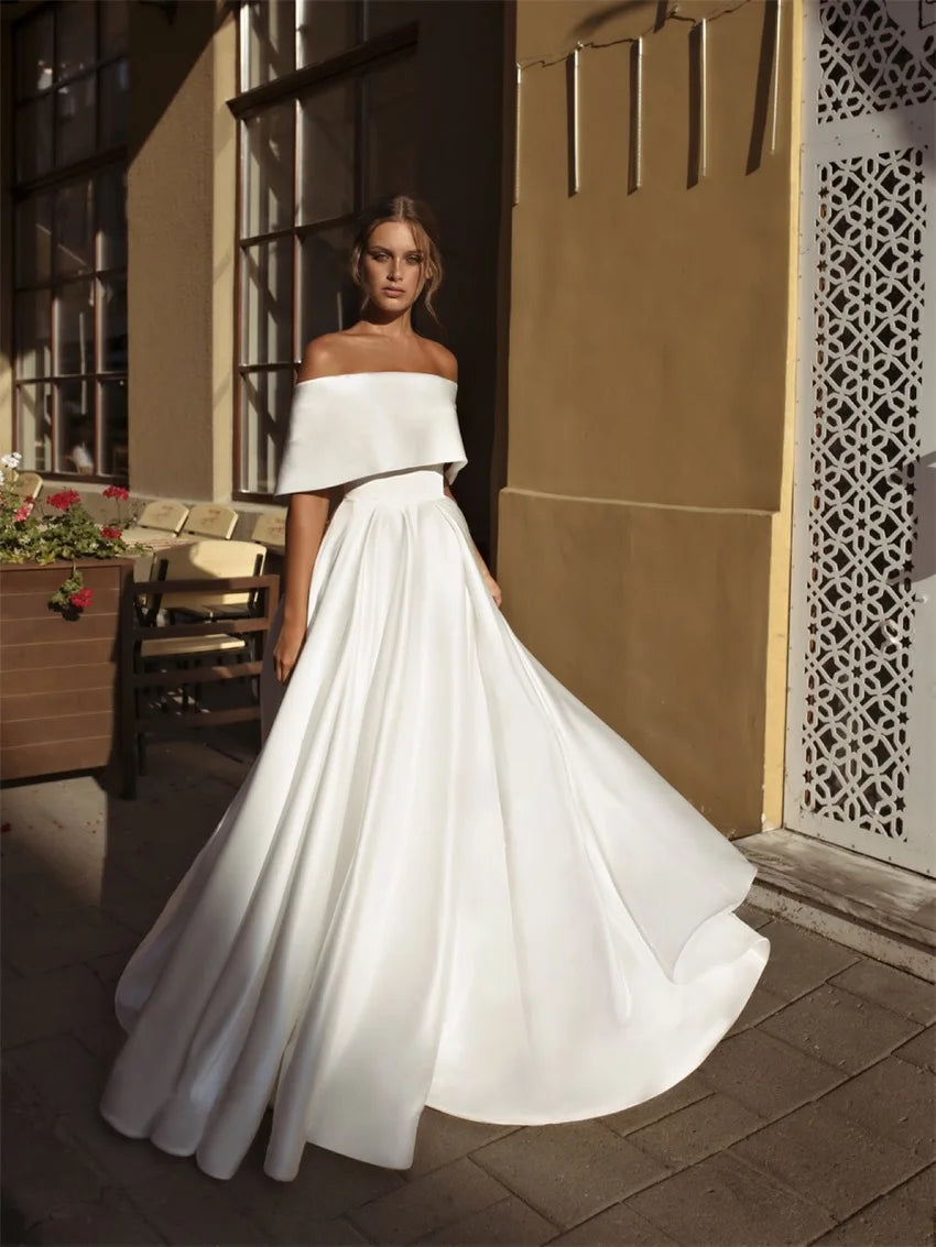 Woman in an off-the-shoulder white wedding gown stands on a sunlit patio with intricate lattice paneling and floral decorations, casting soft shadows on the tiled floor.