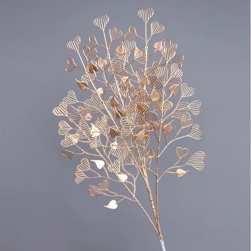 Golden metal branches with intricate heart-shaped leaves clustered together against a gray background, creating a delicate and artistic display.