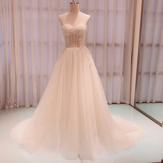 Elegant strapless wedding dress on a mannequin, featuring a lace bodice and a flowing tulle skirt with a subtle train, set against softly lit sheer curtains.
