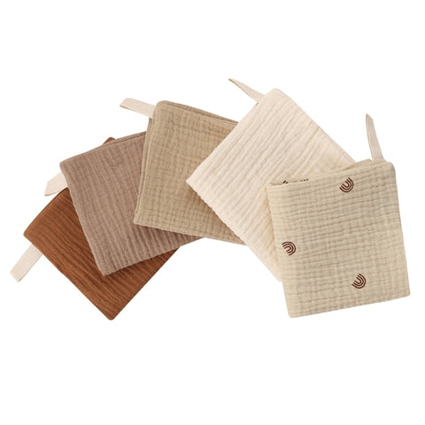 Five square quilted pot holders in shades of brown and cream, one with small rainbow designs, arranged in a fan. Each has a fabric loop for hanging.