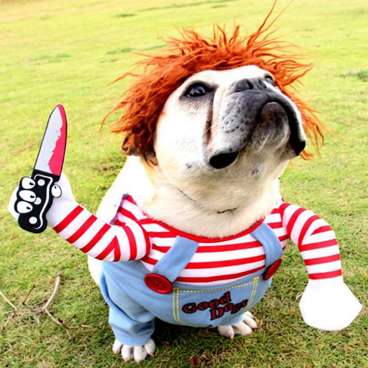 Bulldog dressed in a playful costume resembling a doll, with a red wig, striped outfit, and toy knife, standing on grass.