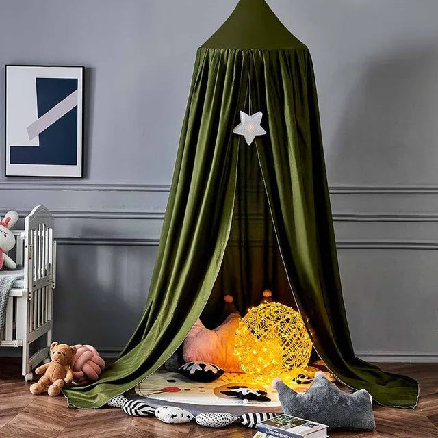 A cozy play area with a green canopy decorated with a star light, plush cushions, a glowing orb, and toys. A crib and framed art are on the left, set against gray walls.