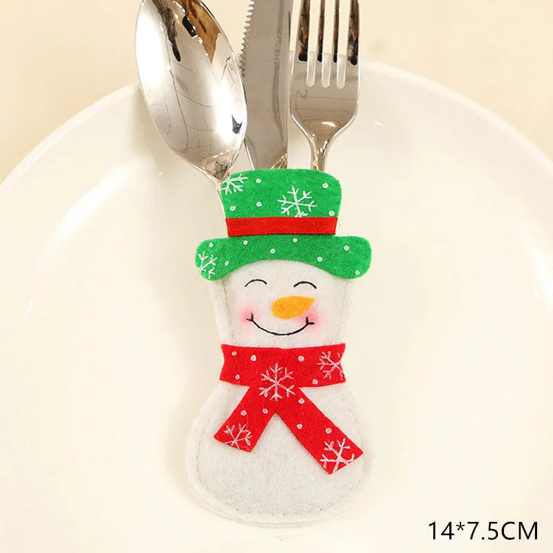 A snowman-shaped cutlery holder in festive colors, featuring a green hat and red scarf with snowflake patterns, holds a spoon, knife, and fork on a white plate.