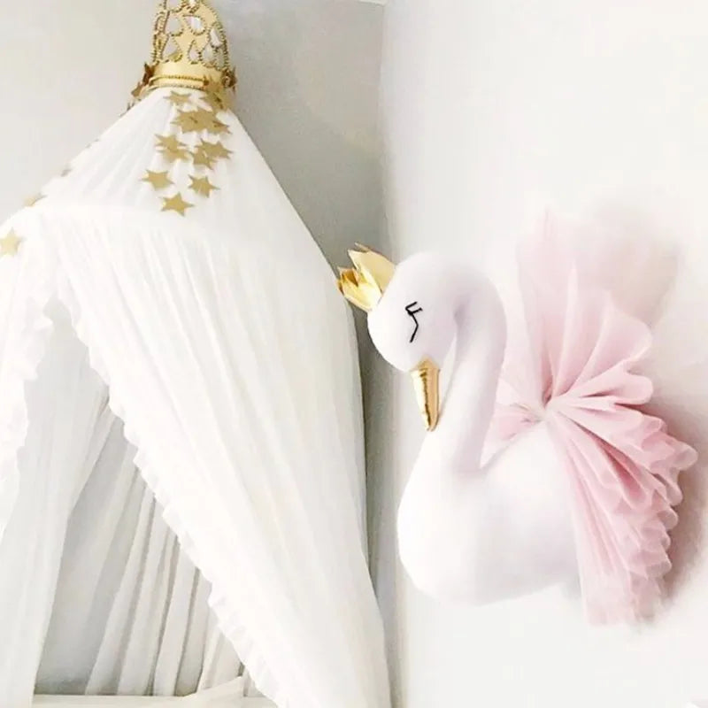 Wall-mounted swan decoration with a gold crown and pink tulle, next to a white canopy adorned with gold stars. Minimalist and elegant nursery decor.