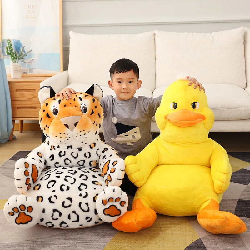 A child sits on a living room floor between two large plush toys: a spotted leopard and a bright yellow duck, with a beige couch and a wooden cabinet in the background.