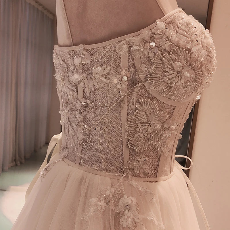 Close-up of an elegant dress bodice featuring intricate floral embroidery and sparkling sequins. The fabric is delicate and softly hued, with tulle details on the skirt.