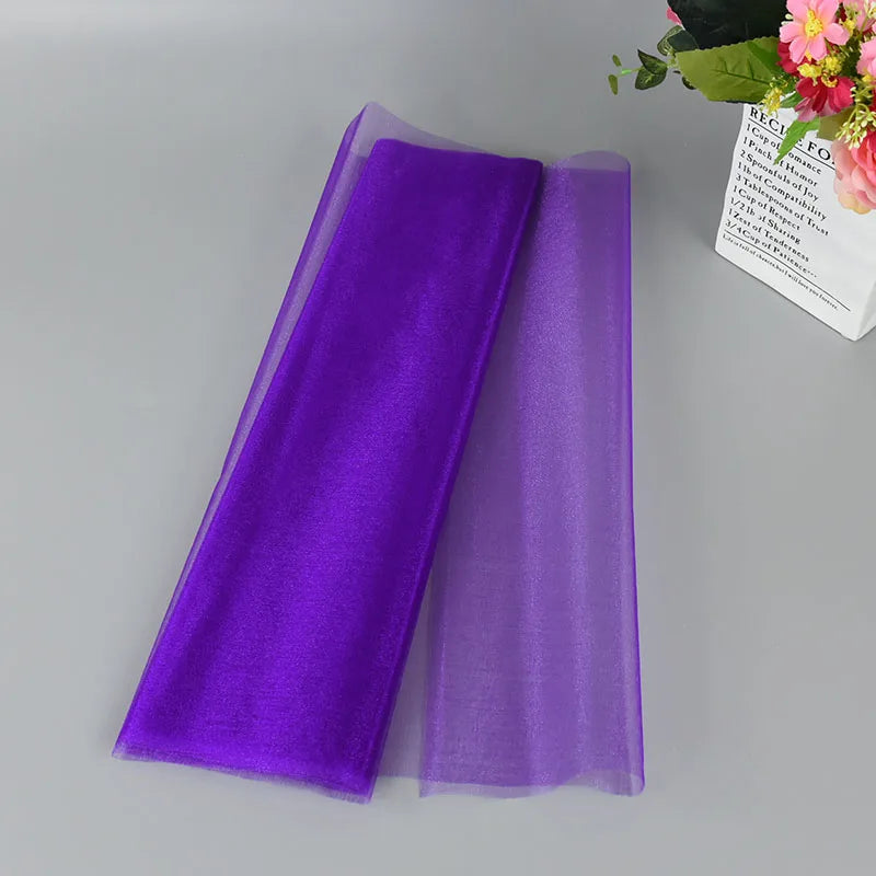 Purple tulle fabric is neatly folded on a gray surface, next to a bouquet of colorful flowers.