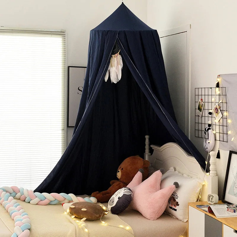 A cozy children's bedroom with a dark blue canopy over the bed, decorated with plush toys, pillows, and a braided blanket. Soft yellow fairy lights add a warm touch.