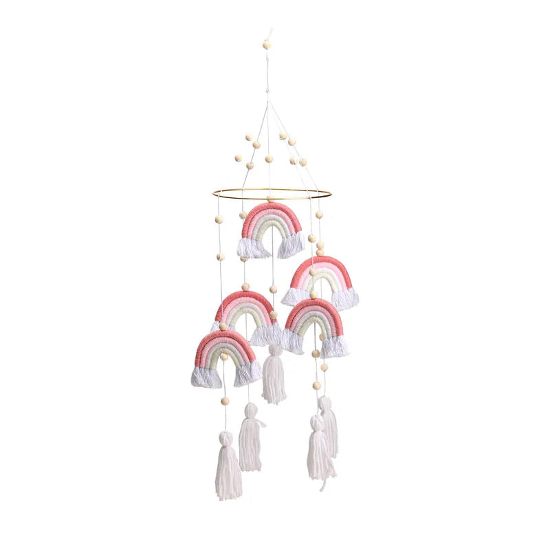 Hanging mobile featuring five pink and white rainbows on strings with tassels and small wooden beads, suspended from a circular wooden ring.