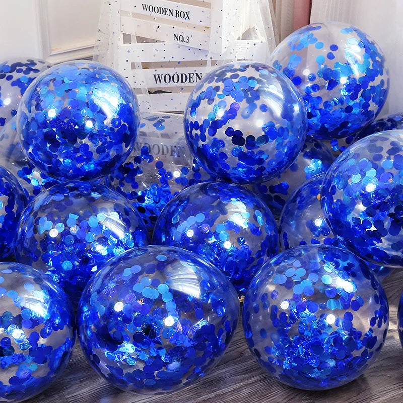 Transparent balloons filled with shiny blue confetti are piled near a decorative wooden box on a wooden floor, creating a festive, celebratory atmosphere.