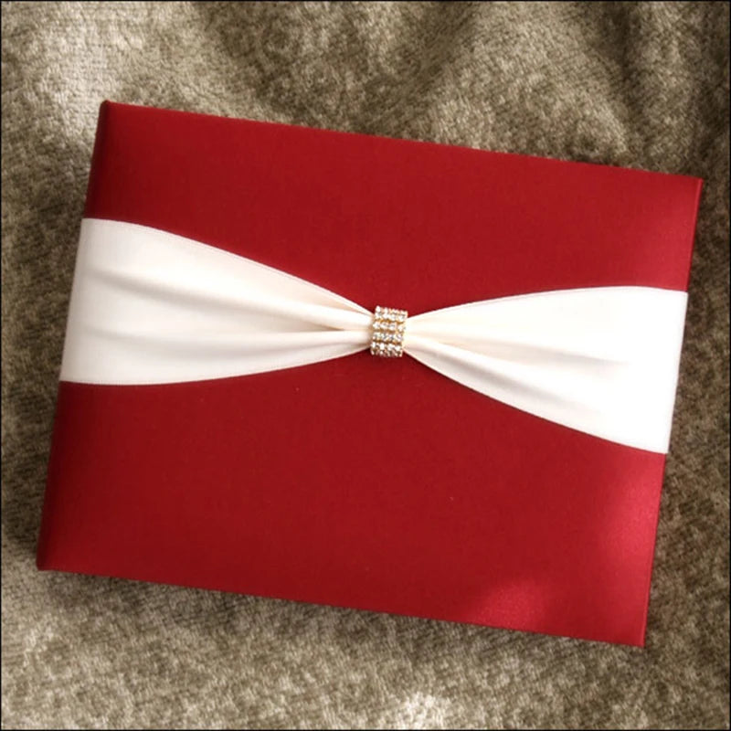 A red gift box with a white ribbon is elegantly tied in the center, adorned with a small gold accent. It rests on a textured gray fabric background.