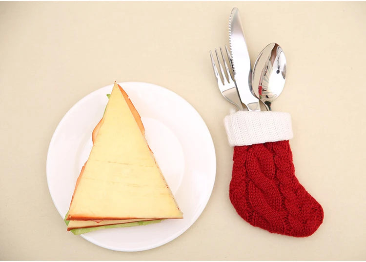 A triangular sandwich on a white plate next to a set of silverware in a festive red and white knit stocking.
