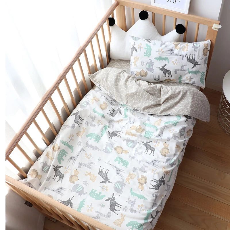 A wooden crib with animal-printed bedding in soft colors. Two pillows with geometric patterns rest on top, and a stuffed crown-shaped pillow is at the head.