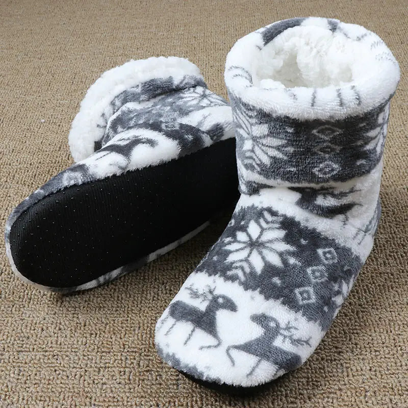 Cozy, fleece-lined slippers with a monochrome reindeer and snowflake pattern, featuring black, non-slip soles, displayed on a textured, beige carpet.