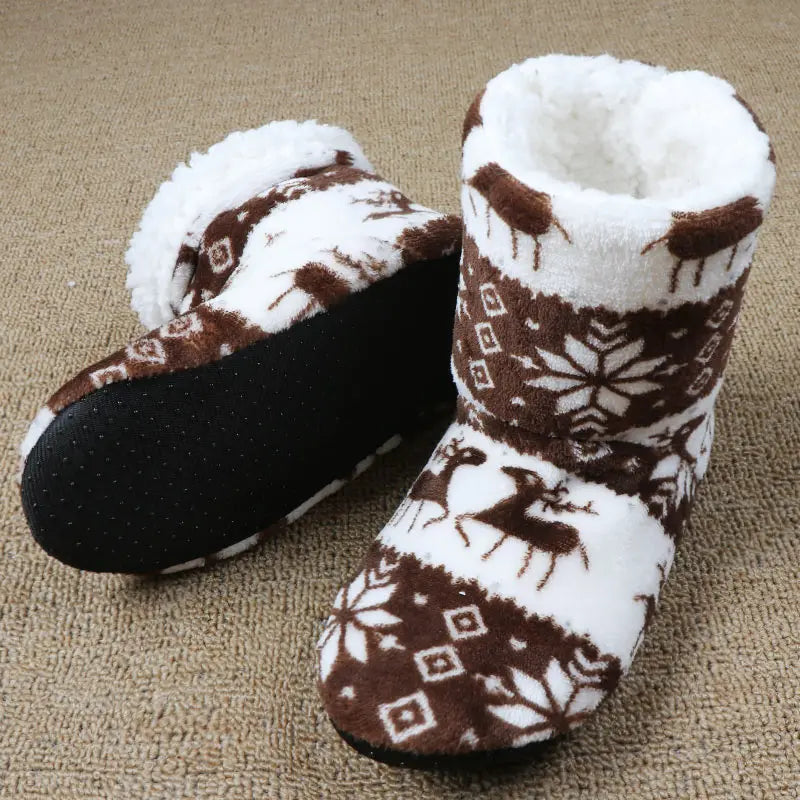 Brown and white fleece slippers with reindeer and snowflake patterns on a beige carpet. One slipper is upright showing the padded lining; the other is on its side displaying the sole.