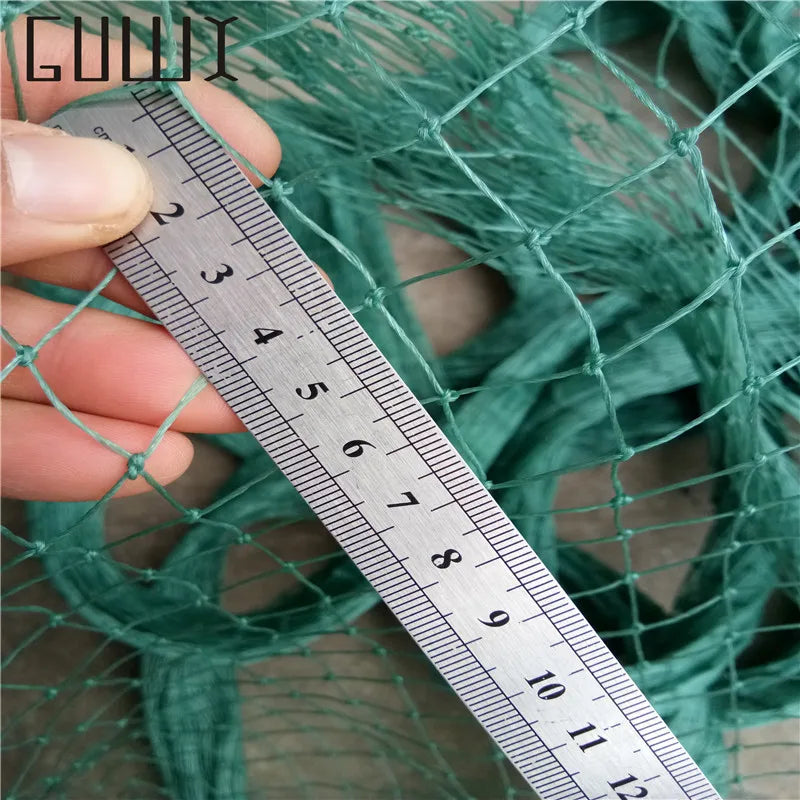 A hand holds a metal ruler measuring the mesh grid of a green net. The ruler displays centimeter markings for scale, indicating the net's dimensions.