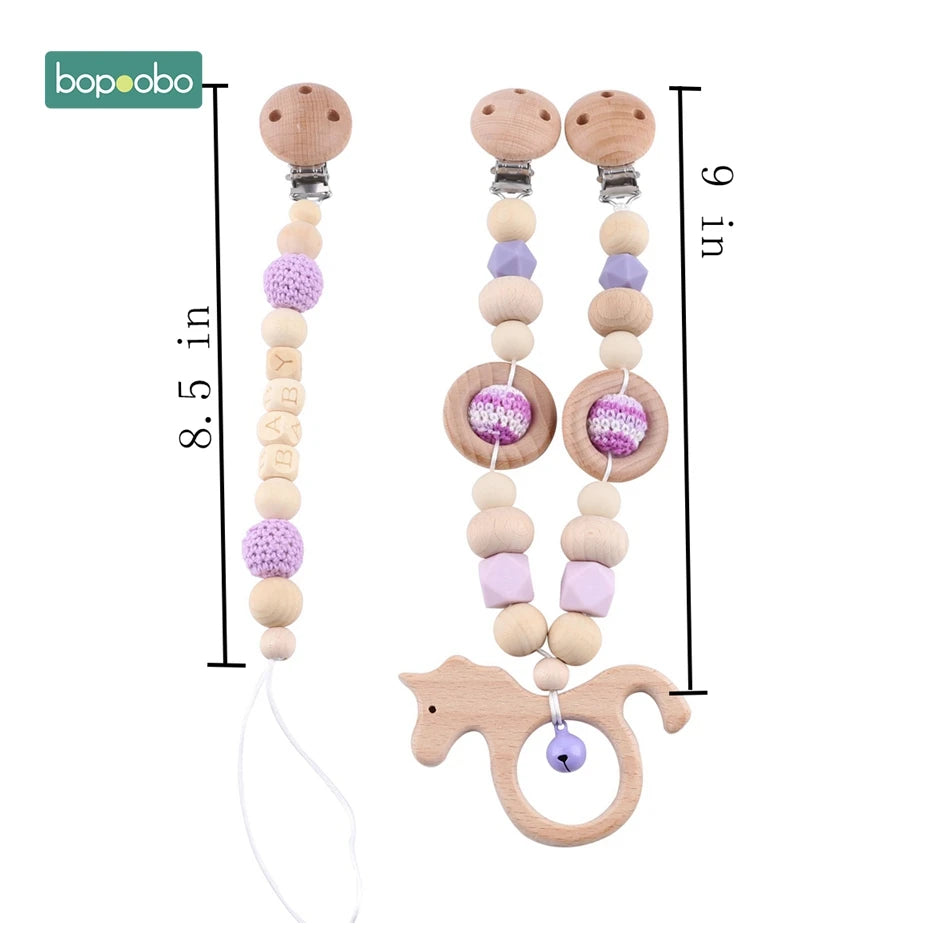 Wooden pacifier clips and teether with crochet beads in purple and beige; one clip measures 8.5 inches, the other 9 inches. Includes a horse-shaped teether with a purple bell.