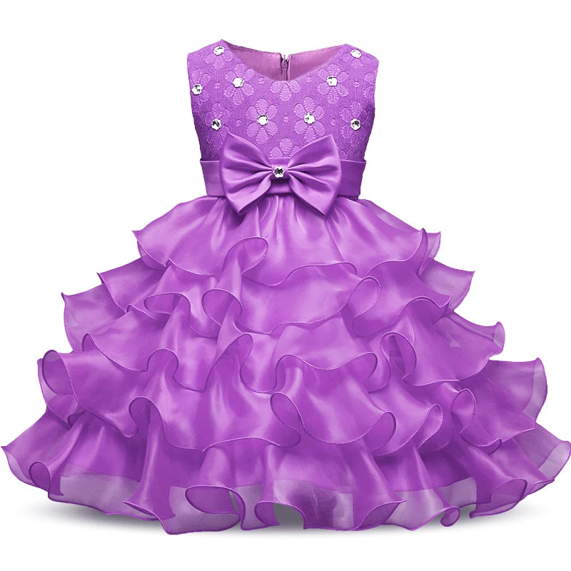 Purple ruffled dress with a lace bodice adorned with floral patterns and gems. The waist features a large bow accent, and the layered skirt creates a voluminous, elegant look.