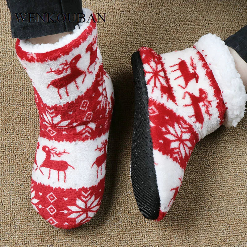 Red and white fleece slippers with reindeer and snowflake patterns, worn by a person on a beige carpet. Black soles provide contrast to the festive holiday design.