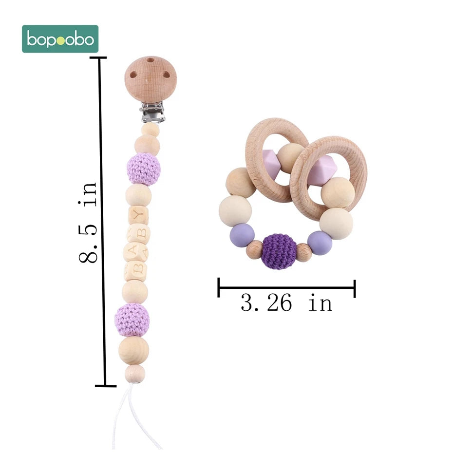 Wooden baby pacifier clip and teether toy set with purple crochet and natural beads. Clip measures 8.5 inches, teether 3.26 inches. Both are from the brand bopoobo.