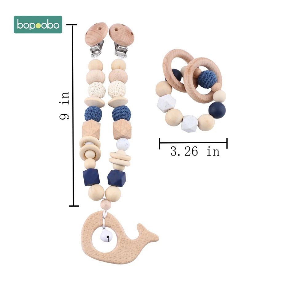 Wooden baby teething set with a pacifier clip (9 inches) and teething ring (3.26 inches). Features blue, white, and natural wooden beads, with a whale and bell.