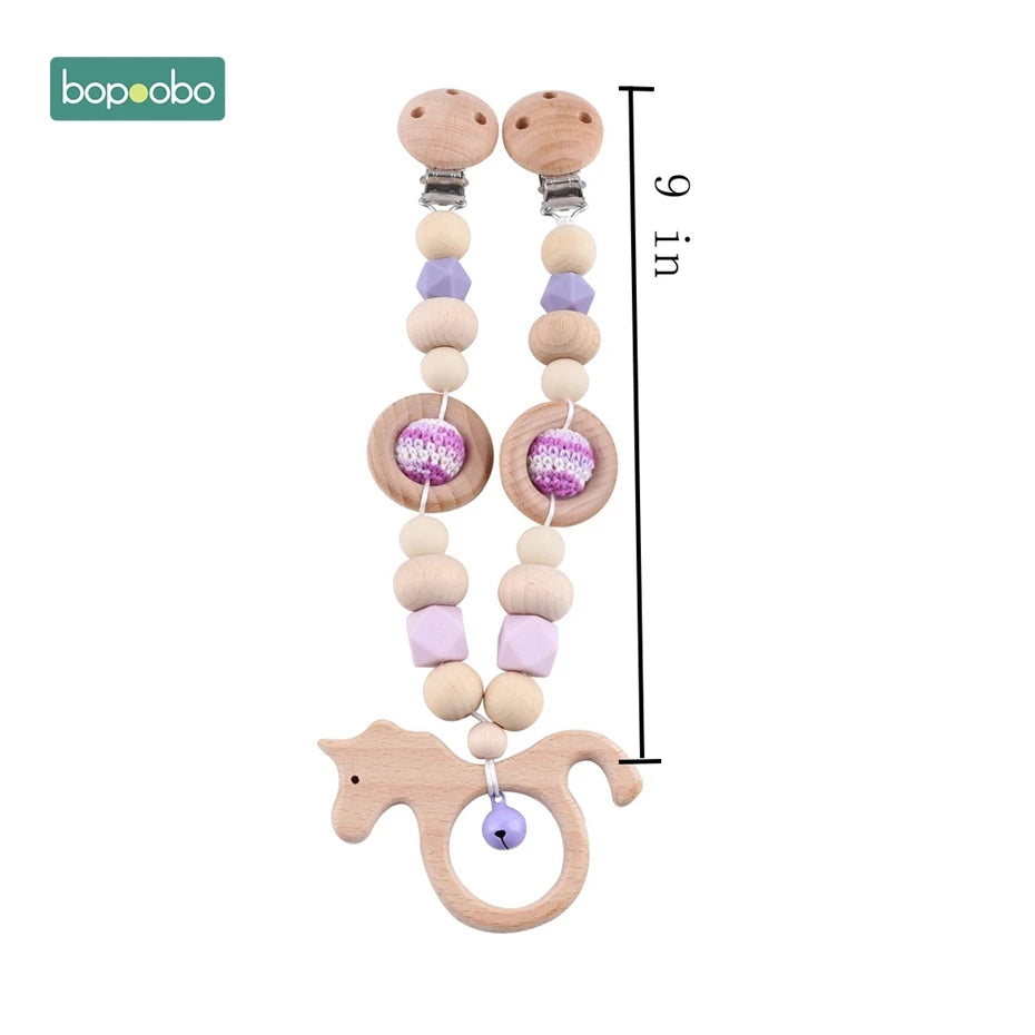 Wooden teether with smooth beads, lavender crochet accents, and a cute horse shape with a small bell attached. Measures 9 inches in length. Brand logo "bopoobo" visible.