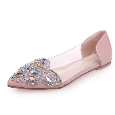 Pink flat shoe with a pointed toe, featuring transparent sides and adorned with intricate multicolored gemstone decorations on the front.