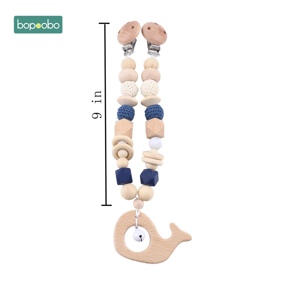 Wooden pacifier clip with blue and natural beads, measuring 9 inches. Features a whale-shaped teether and secure metal clasp, ideal for babies.