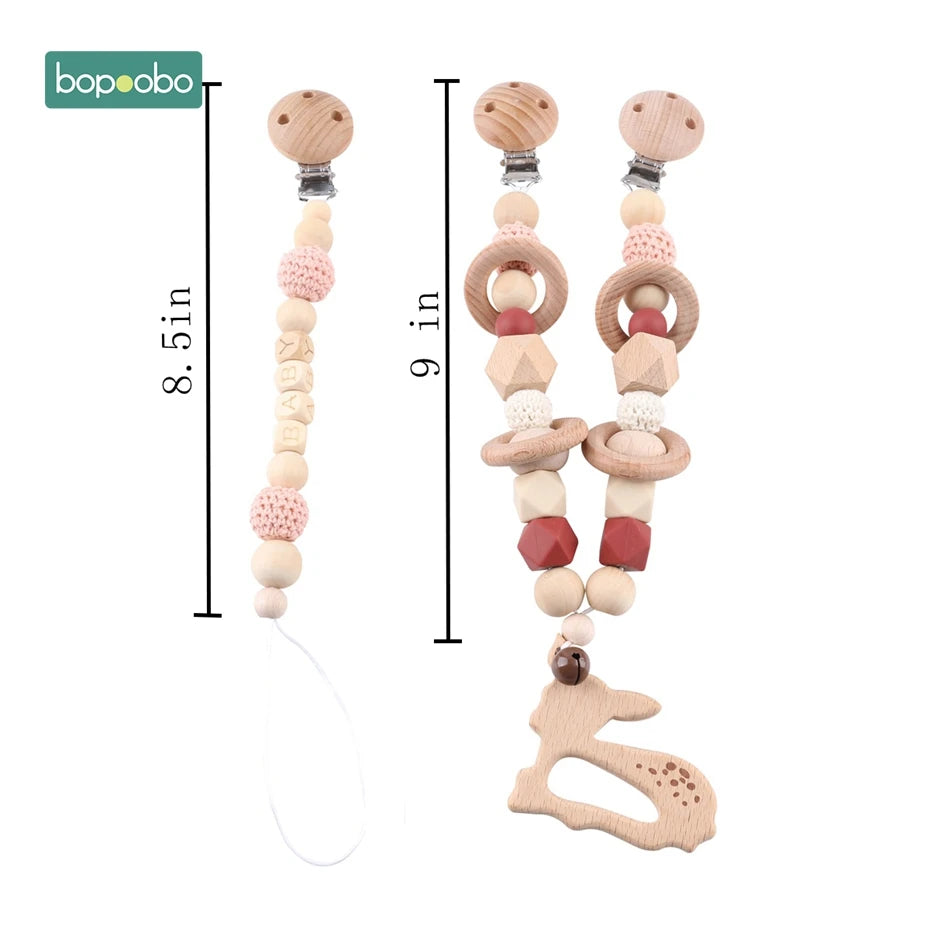 Two pacifier clips made of wooden beads and crochet accents. One measures 8.5 inches with "BABY" beads, the other is 9 inches with a wooden rabbit charm and geometric beads.
