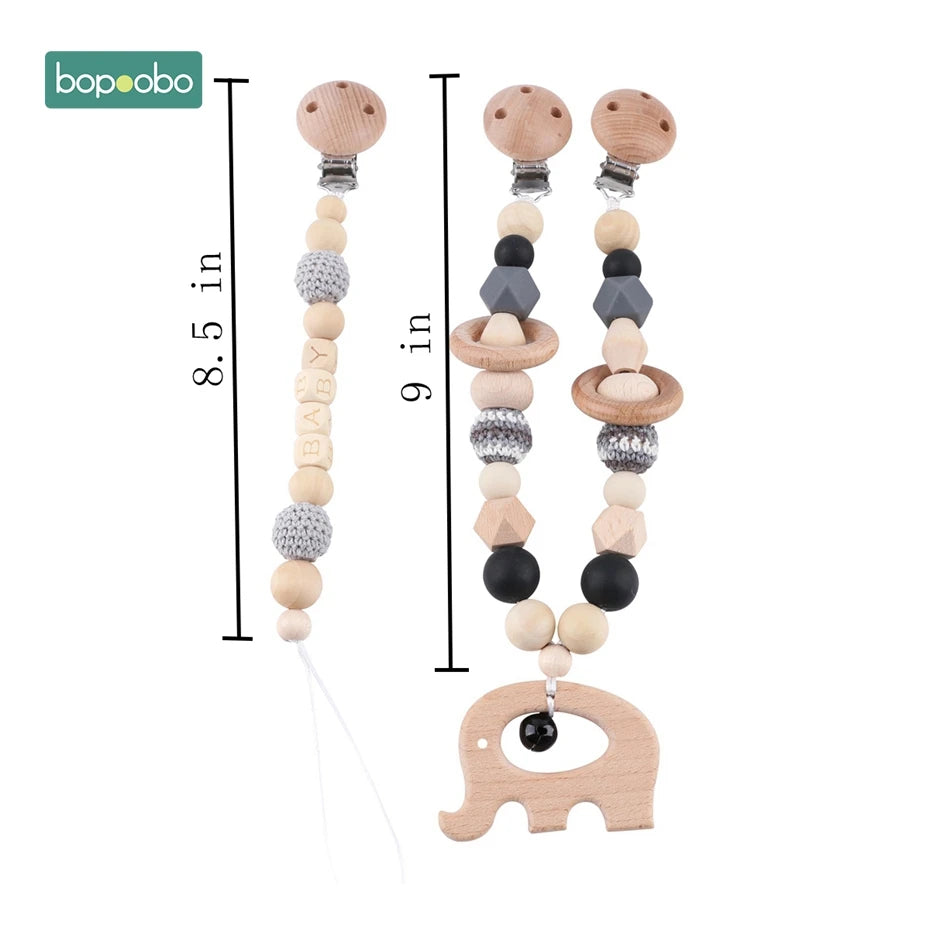 Three beaded pacifier clips: one with "BABY" beads, another with a wooden ring, and the third with a wooden elephant. Lengths are 8.5 and 9 inches.