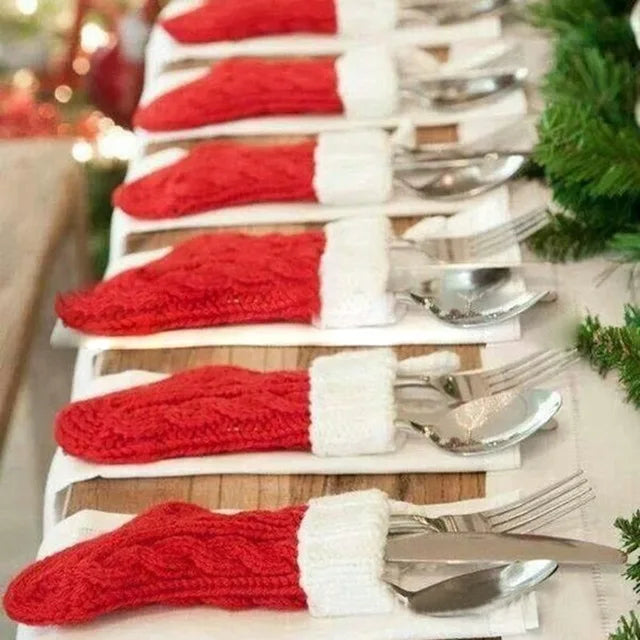 Festive table setting with cutlery placed in red and white Santa hat holders on napkins, surrounded by greenery for a holiday-themed arrangement.