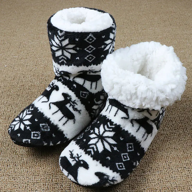 Cozy black and white fleece slippers with a winter pattern of snowflakes and reindeer. They have a fluffy white interior, perfect for keeping feet warm on a cold day.