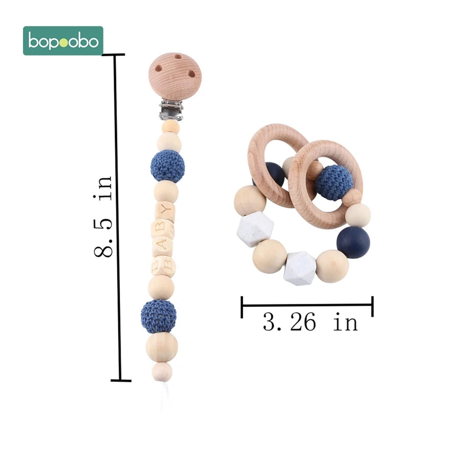 Wooden pacifier clip chain and teething toy by bopoobo. The chain measures 8.5 inches and features blue beads and "BABY" letters. The teether is 3.26 inches with rings and beads.
