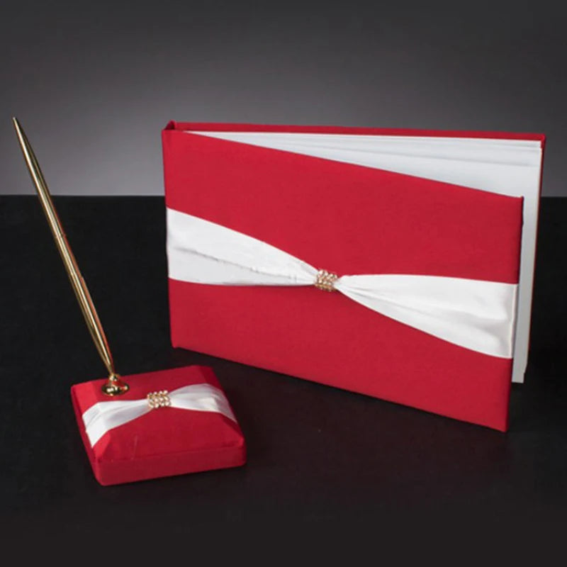 Red guestbook with a white ribbon and gold accent, paired with a matching red and white pen holder featuring a gold pen, set against a dark background.