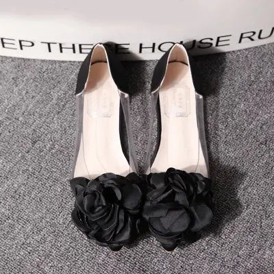 Elegant black peep-toe flats adorned with large black rose embellishments, resting on a gray textured surface.