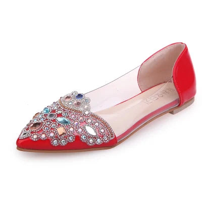 Red pointed-toe flat shoe with a transparent side, adorned with colorful rhinestones and pearls on the front, creating an ornate and elegant design.