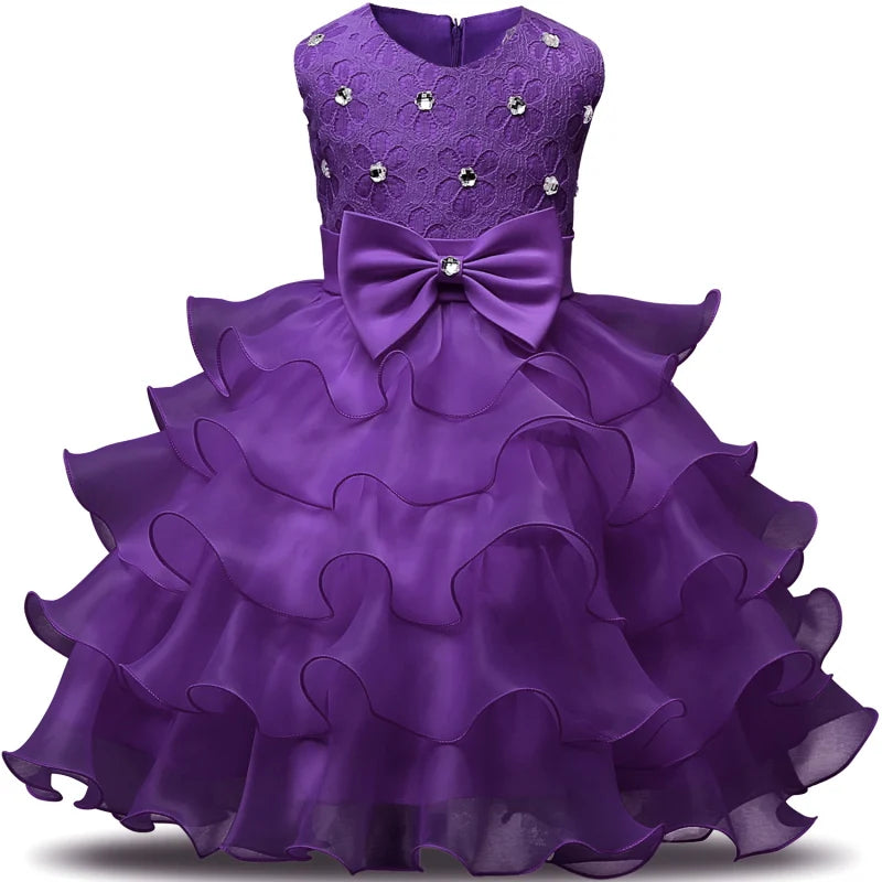 Purple ruffled dress for a child, featuring a lacy bodice adorned with small floral embellishments and a large bow at the waist.