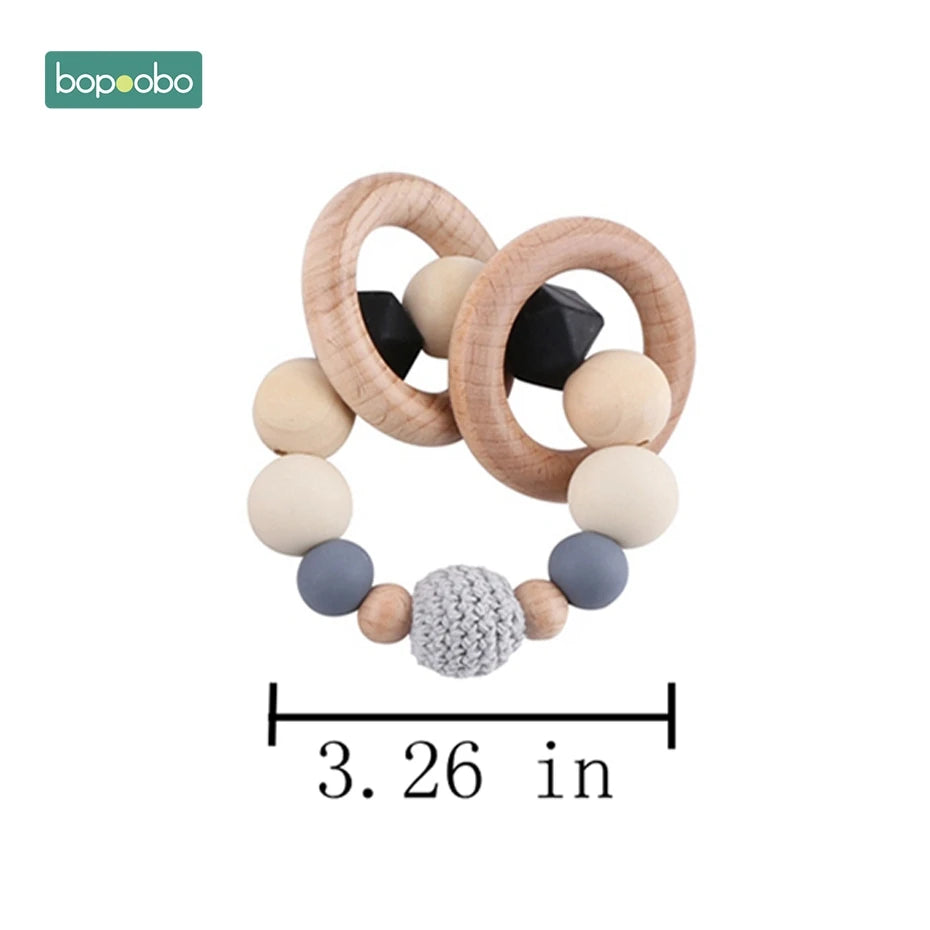 Wooden and silicone baby teething ring with wooden circles, monochrome beads, and a crocheted bead, measuring 3.26 inches. Brand logo "bopoobo" in the corner.