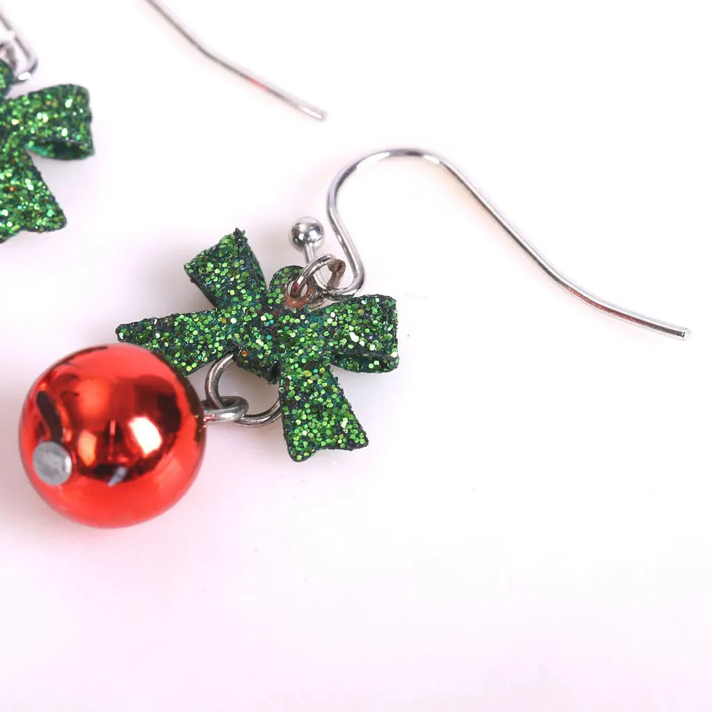 Close-up of festive earrings featuring a glittery green bow and a shiny red bauble, hanging from a silver hook.