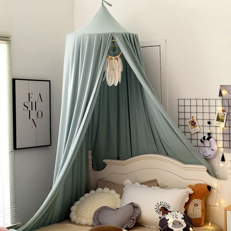 Cozy bedroom with a pastel canopy over a bed adorned with decorative pillows. A dreamcatcher hangs from the canopy. Soft lighting and a fashion poster enhance the ambiance.
