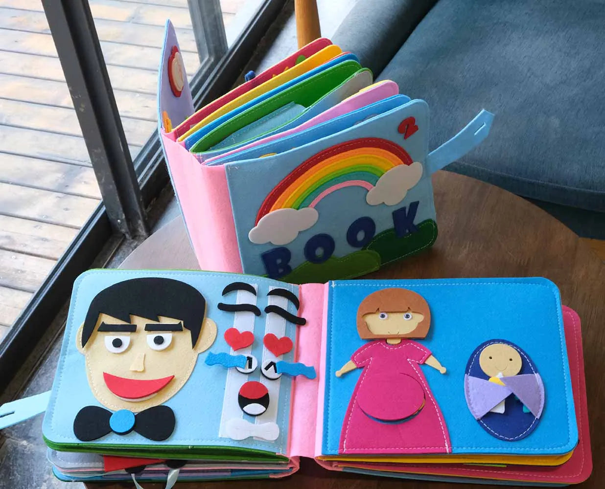 Colorful felt children's book with page designs of a man and comic face on one page, and a woman with a baby in pink dress and blue background on the other. Covers show a rainbow and "Book".