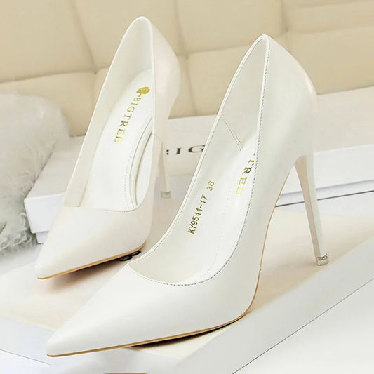 Elegant white stiletto heels with pointed toes, displayed on a beige surface. The shoes have branding inside and are designed with slender, high heels.